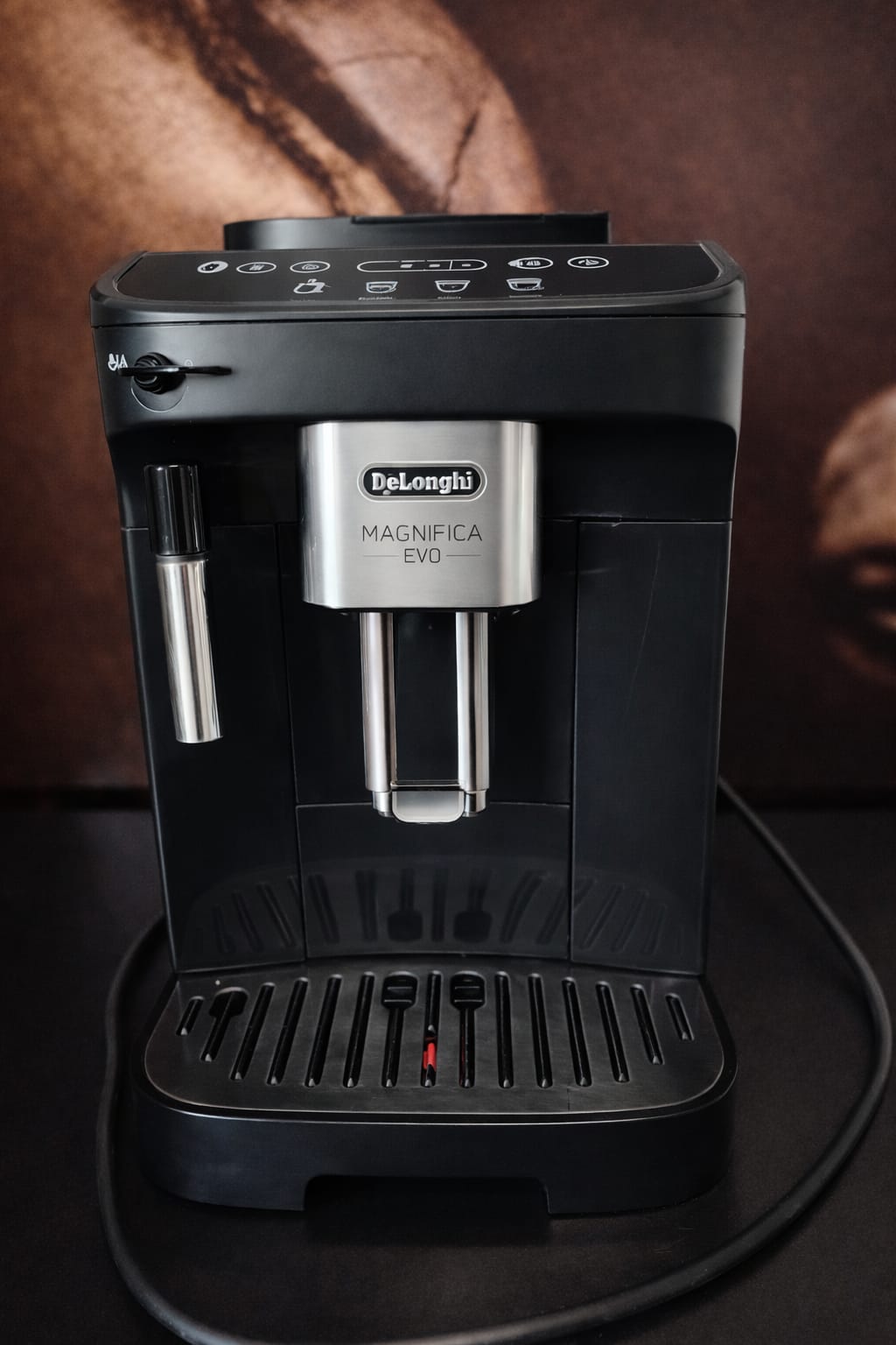 Kompaktowy czarny ekspres automatyczny De'Longhi Magnifica Evo ECAM290.22.B z podświetlanym panelem sterowania soft touch z kolorowymi ikonami i ręczną dyszą cappuccino, widok z przodu na białym tle