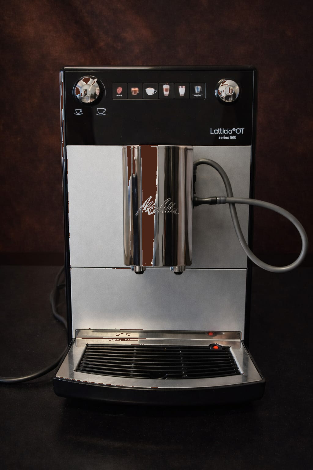 Srebrny ekspres automatyczny Melitta Latticia OT F300-101 z czarnym panelem sterowania, podświetlanymi przyciskami do napojów mlecznych i czarnej kawy, widok z przodu na białym tle